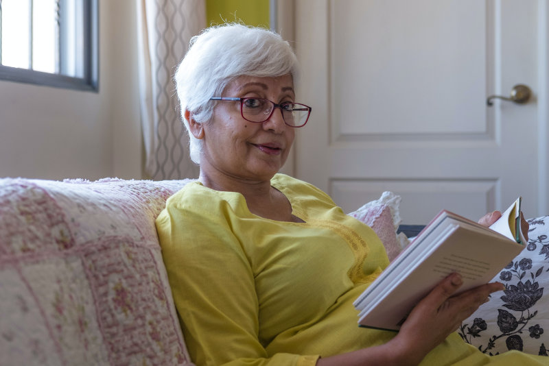 confident looking, older lady holder a book, wearing glasses, and smiling at camera